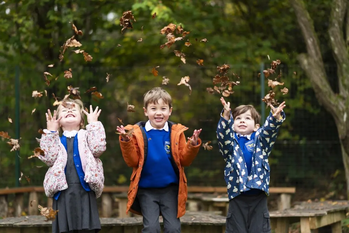 Three children throwing autumn leaves into the air in the school grounds