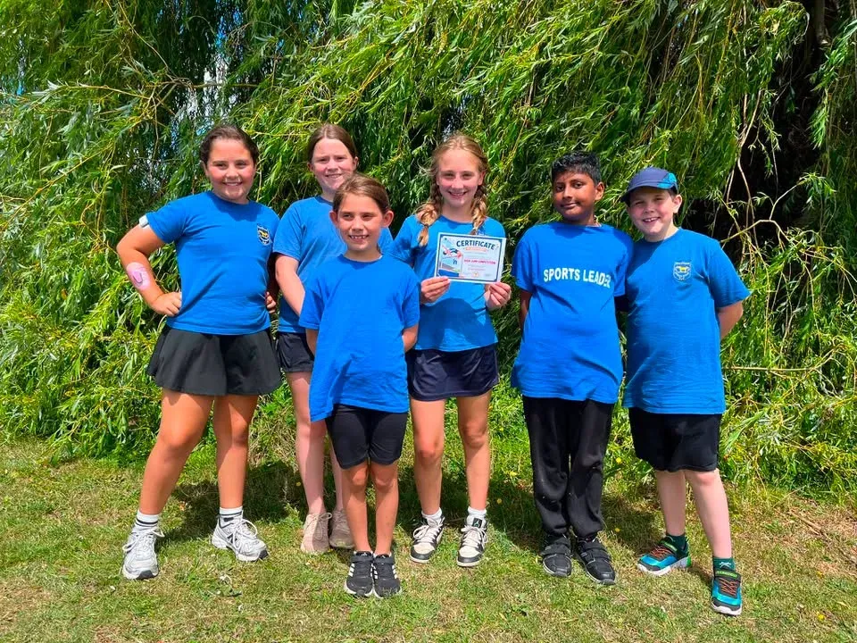 Six pupils in blue sports leader t-shirts standing proudly on the field, one holding a certificate