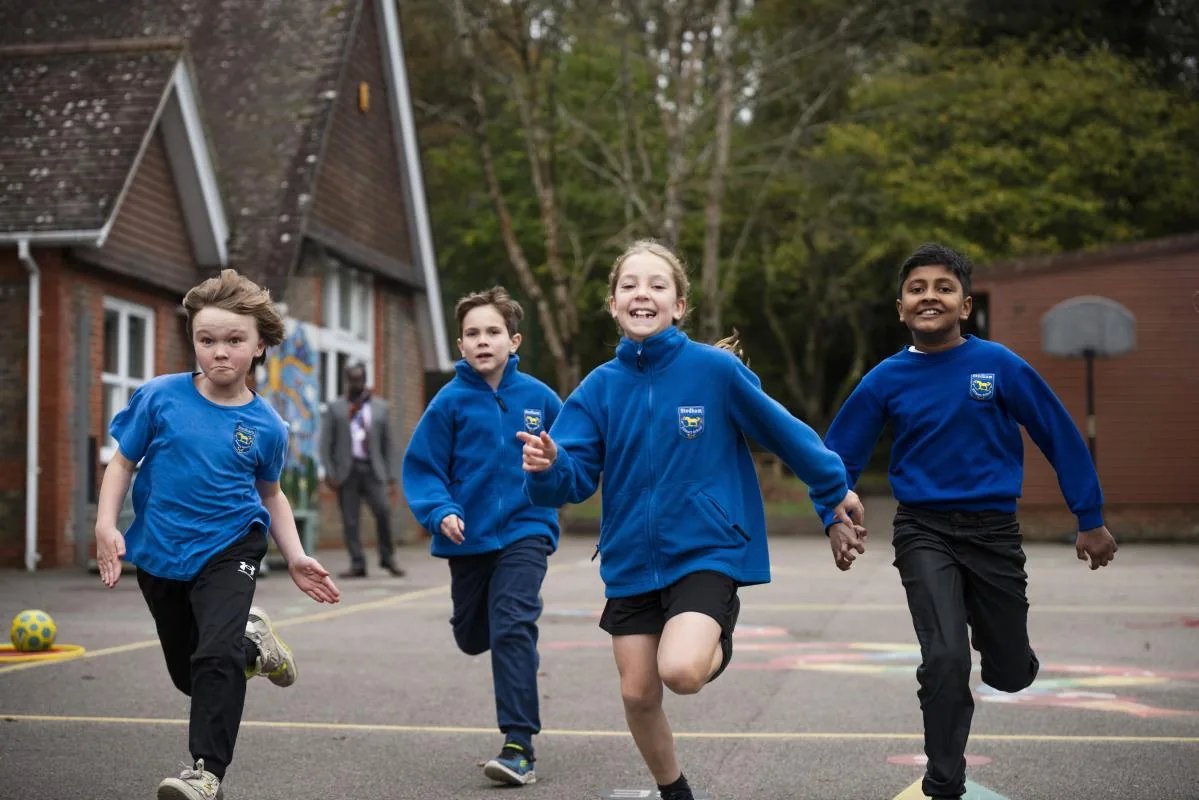 Children in blue fleeces running happily across the playground